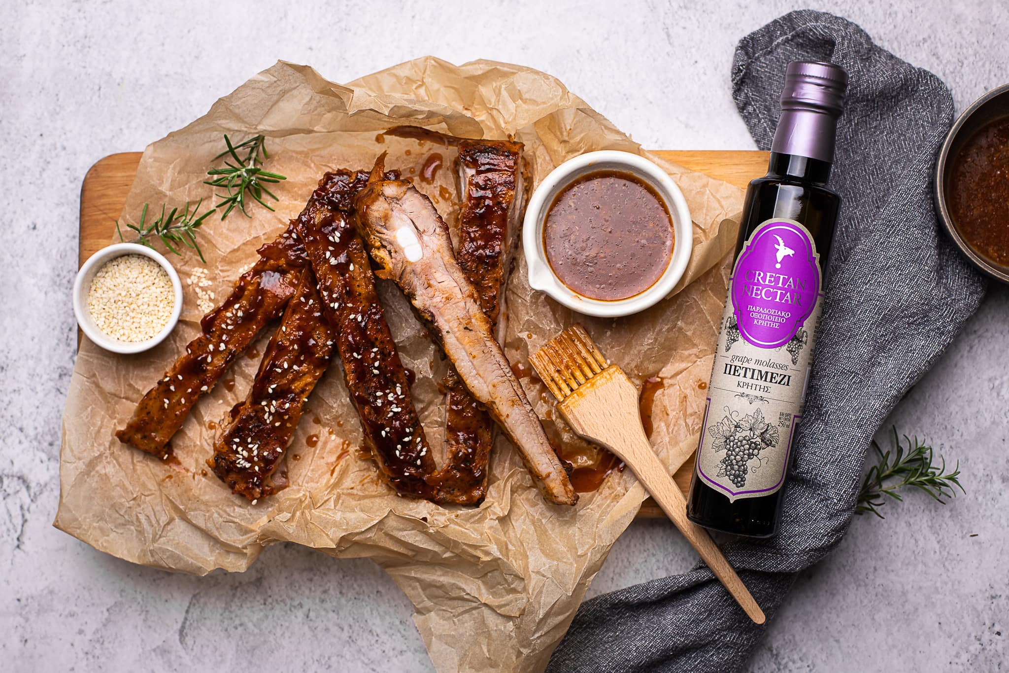 Hallil laual on küpsetuspaberil glaseeritud lahti lõigatud searibid. Neist paremal kauss kastmega, toidupintsel ja pudel viinamarjamelassiga ehk petimeziga.