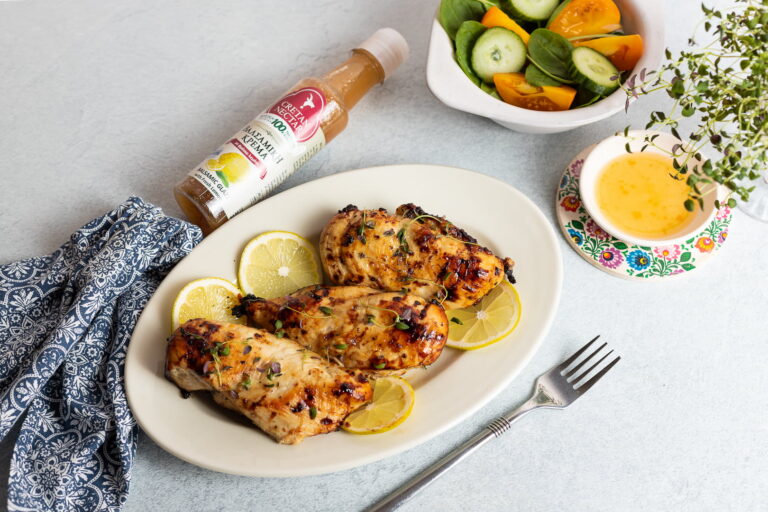 Valgele lauale on asetatud valge taldrik marineeritud kanafileetükkidega, mille kõrvale on laotatud lõigatud sidruniviilud. Taldrikust paremal on hõbedane kahvel ja vasakul Cretan Nectar sidruniga palsamikreemi pudel. Selle kohal on valges kausis värske salat.