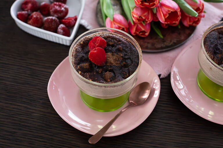 Kreemjas šokolaadimagustoit klaasis, peal šokolaadipuru ja värsked vaarikad, serveeritud roosal taldrikul.